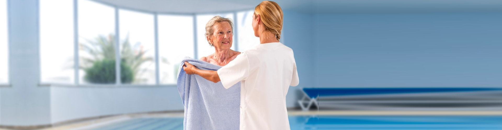 Caregiver helping elderly woman to get out of swimming pool with bath towel